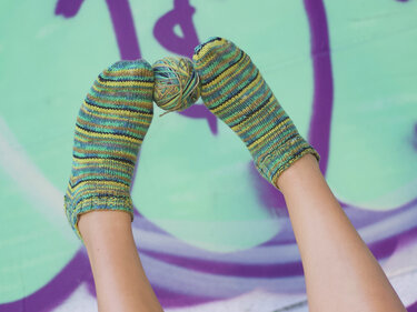 Gestrickte kurze Socken mit Streifenmuster und sichtbarem Garnverlauf, Garnknäuel zwischen den Zehen