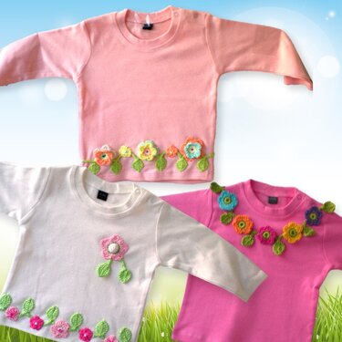 Drei Kinderpullover in Pastell- und kräftigen Farben mit gehäkelten Blumen- und Blatt-Applikationen an Saum und Halsausschnitt