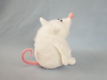 Flauschige weiße Amigurumi-Maus mit rosa Nase, rosa geringeltem Schwanz und schwarzen Augen vor hellem Hintergrund