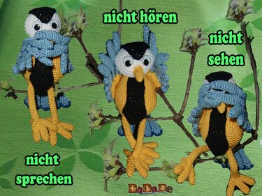 Drei gehäkelte Amigurumi‑Vögel in Blau, Gelb und Schwarz auf Zweigen in den Posen nicht hören / nicht sehen / nicht sprechen