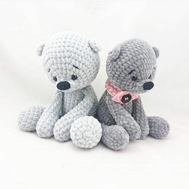 Zwei gehäkelte graue Teddys, einer mit rosa Halsband, sitzend