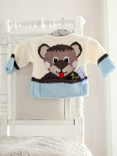 Gestrickter Baby-Pullover creme und hellblau mit eingestricktem Bärenmotiv an weißem Stuhl