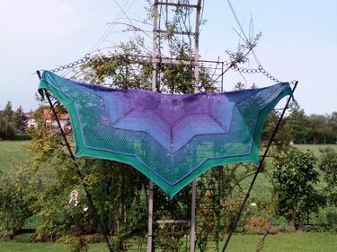 Triangular knitted shawl with purple, blue and green gradient displayed outdoors