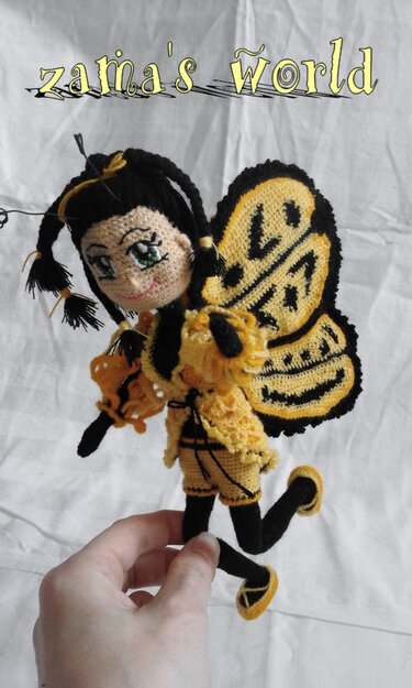 Gehäkelte Amigurumi-Puppe mit gelb-schwarzem Insektenkostüm, von einer Hand gehalten