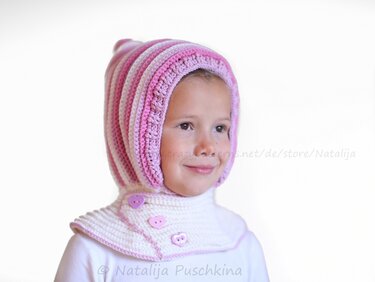 Kind trägt gehäkelte rosa-weiß gestreifte Kapuzenmütze mit herzförmigen Knöpfen