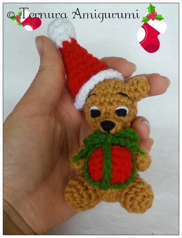 Mini amigurumi teddy bear in hand wearing a Santa hat and holding a tiny gift