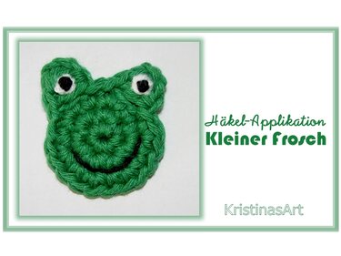 Grüne gehäkelte Frosch-Applikation mit weißen Augen und schwarzem Lächeln