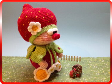 Gehäkelte Erdbeer-Amigurumi mit rotem Hut, Blüte und kleinem Korb auf grüner Miniwiese