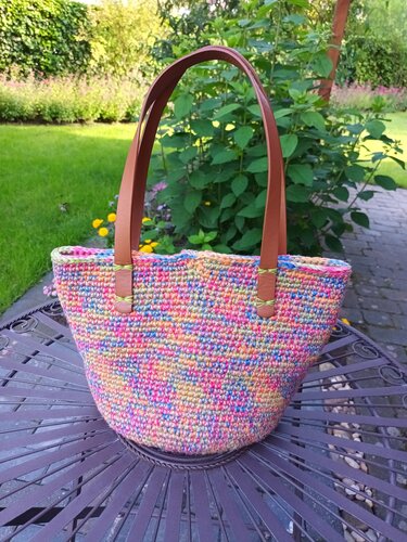 Gehäkelte Henkeltasche mehrfarbig mit braunen Tragegriffen auf einem Gartentisch