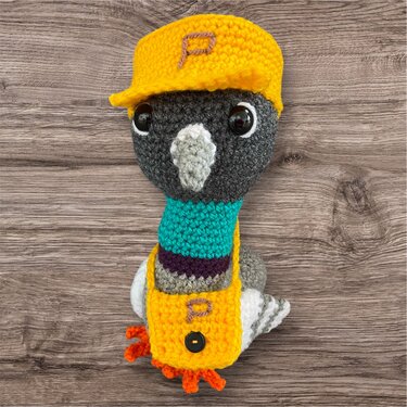 Gehäkelte Amigurumi-Taube in Grau, Weiß und Türkis mit gelber Schirmmütze und Umhängetasche mit eingesticktem P.
