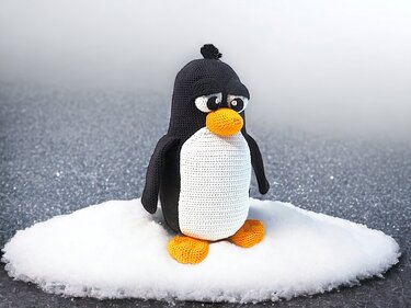 Close view of a crocheted penguin amigurumi highlighting white belly and orange beak