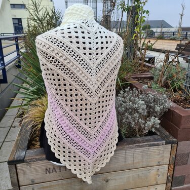 Crocheted triangle shawl in white, beige and pink gradient with lace and bobble stitches on a mannequin.