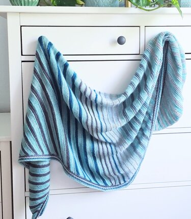 Gestricktes Dreieckstuch mit Streifen in Blau-, Türkis- und Grautönen auf weißer Kommode