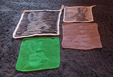 Vier handgestrickte Topflappen mit Hasenmotiven in Schwarz-Weiß, Creme, Grün und Rosé auf dunklem flauschigem Untergrund