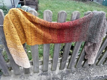 Langer gehäkelter Schal mit gelb-rot-grauem Farbverlauf auf einem Holzzaun