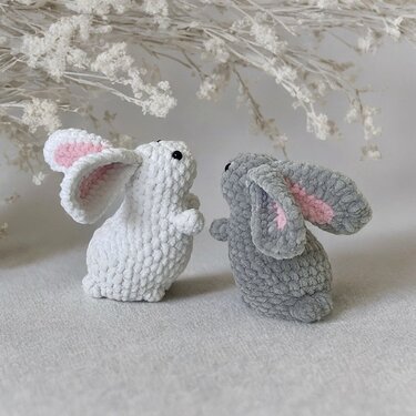 Zwei Amigurumi-Häschen, eines weiß, eines grau, mit rosa Innenohren vor hellem Hintergrund.