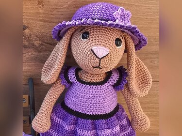 Crocheted amigurumi rabbit with floppy ears wearing a purple dress and matching hat