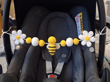 Yellow and white crocheted garland with a striped bee and two daisies tied across a dark infant car seat handle