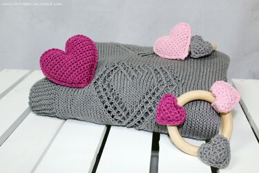 Grau gestrickte Babydecke mit eingestricktem Herzmuster, gehäkelten Herzen und Holzring