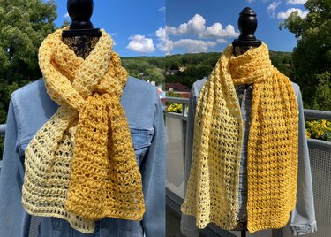 Zweifarbiger gehäkelter Schal in Hell- und Dunkelgelb mit offenem Muster auf einer Schaufensterpuppe, dazu Jeansjacke im Freien.