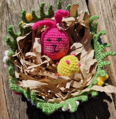 Gehäkeltes Körbchen mit grüner Blumenborte, gefüllt mit Papierschnipseln, einem Häkel-Osterhasen und einem Küken