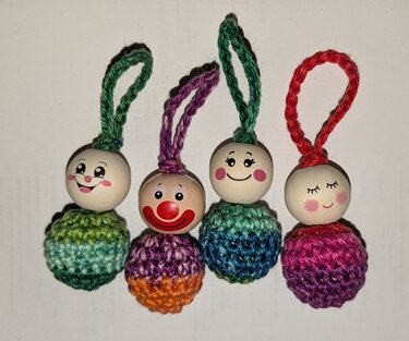 Nahaufnahme von vier handgemachten Anhängern mit bemalten Holzperlenköpfen und gehäkelten Körpern in bunten Garnen.