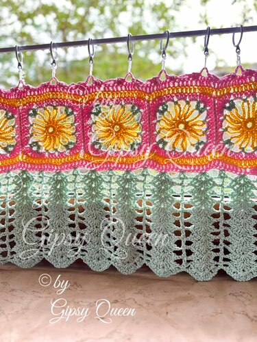 Bunte gehäkelte Scheibengardine mit Sonnen-Granny-Squares und mintgrünem, gewelltem Unterteil an einer Stange.