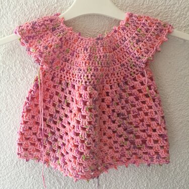 Rosa gehäkeltes Babykleid mit kurzen Ärmeln und bunten Sprenkeln an weißem Kleiderbügel