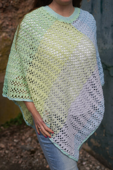 Gehäkelter Pastell-Poncho mit offener Maschenstruktur über Jeans