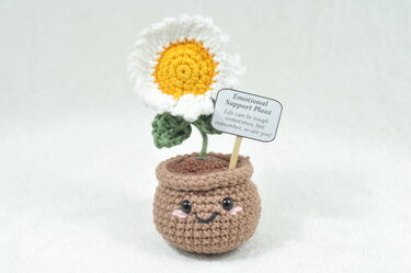 Cheerful crocheted daisy in a small pot with a sign that reads 'Emotional Support Plant'.