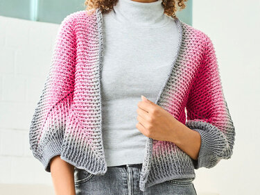 Gehäkelte kurze Damenjacke mit Farbverlauf von Grau zu Pink, offen getragen
