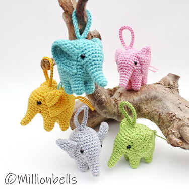 Five small crocheted elephant keychains in pastel colors hanging from a piece of driftwood