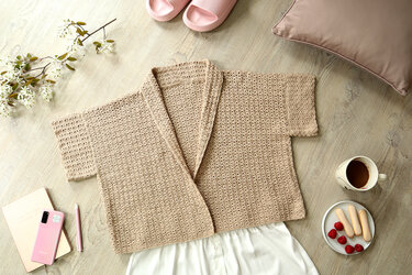 Beige short-sleeve crochet women's jacket with shawl collar laid flat on a wooden surface