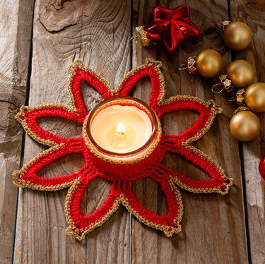 Rotes, gehäkeltes Stern-Deckchen mit goldener Umrandung und Teelicht auf Holz, umgeben von Weihnachtskugeln