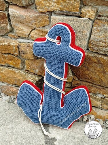 Gehäkeltes Anker-Kissen blau mit roter Kante und weißem Tau vor Natursteinwand