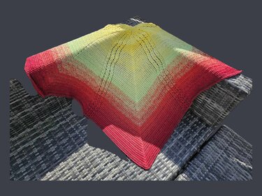 Gehäkeltes Dreieckstuch in Gelb, Hellgrün und Rot mit Lochmuster auf grauem Geflecht.