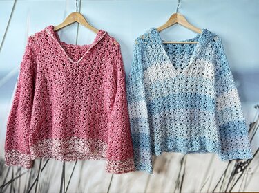 Zwei gehäkelte Kapuzenpullover an Kleiderbügeln, rosa und blau-weiß gestreift; V-Ausschnitt und offenes Lochmuster