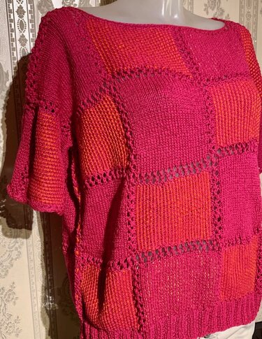 Gestrickte Tunika in Rot- und Pinktönen mit Quadratmuster auf einer Schaufensterpuppe
