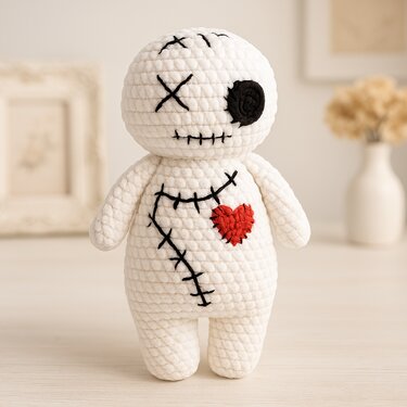Gehäkelte weiße Amigurumi-Puppe mit schwarzen Kreuzstichen und rotem Herz