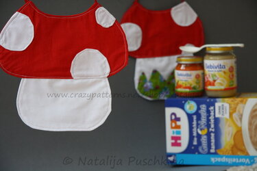 Zwei pilzförmige Babylätzchen in Rot und Weiß mit applizierten weißen Punkten, arrangiert neben Gläsern mit Babynahrung