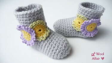 Gehäkelte graue Babyschuhe mit pastellfarbener Blumenapplikation