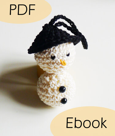 Mini gehäkelter Schneemann-Amigurumi mit schwarzer Mütze, zwei schwarzen Knöpfen und oranger Nase, dazu die Texte 'PDF' und 'Ebook'
