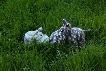 Zwei gehäkelte Nilpferd-Amigurumi im hohen grünen Gras, ein helles und ein gemustertes