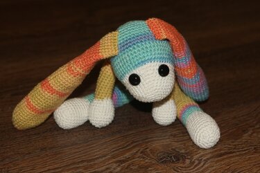 gehäkelter mehrfarbiger Amigurumi-Hase mit langen Ohren auf Holzboden