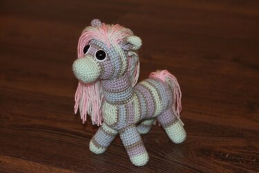 Gehäkeltes Amigurumi-Pony mit rosa Mähne und pastellgestreiftem Körper