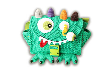 Green crocheted monster-shaped shoulder bag with a large button eye, small stalk eye, red tongue, white teeth, colorful horns, buckle closure and small feet.