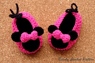 Nahaufnahme pinker gehäkelter Babyschuhe mit schwarzen Ohren und Schleifen