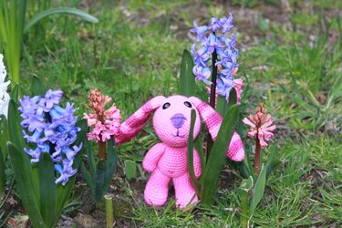 Rosa gehäkelter Amigurumi-Hase mit langen Ohren zwischen blauen und rosa Hyazinthen im Gras