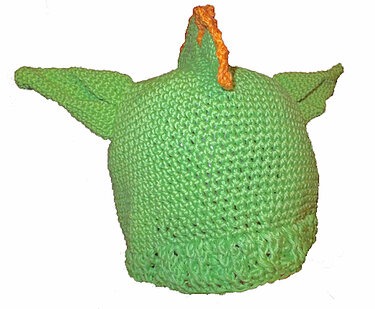Grüne gehäkelte Drachenmütze mit spitzen Ohren und orangefarbenem Zackenkamm auf weißem Hintergrund
