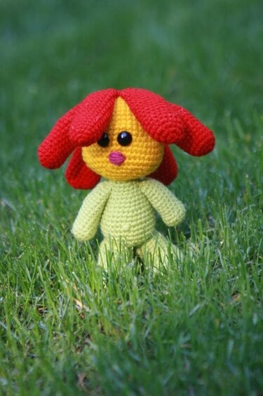 Gehäkelte Amigurumi‑Puppe mit roten Haaren und grünem Körper im Gras